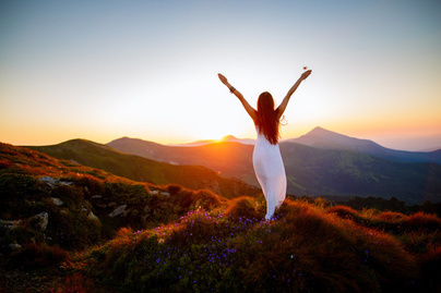 Mujer de espalda abriendo los brazos mirando hacia el horizonte en la montaña