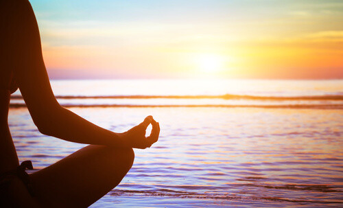 Mujer meditando frente al mar y a la puesta del sol